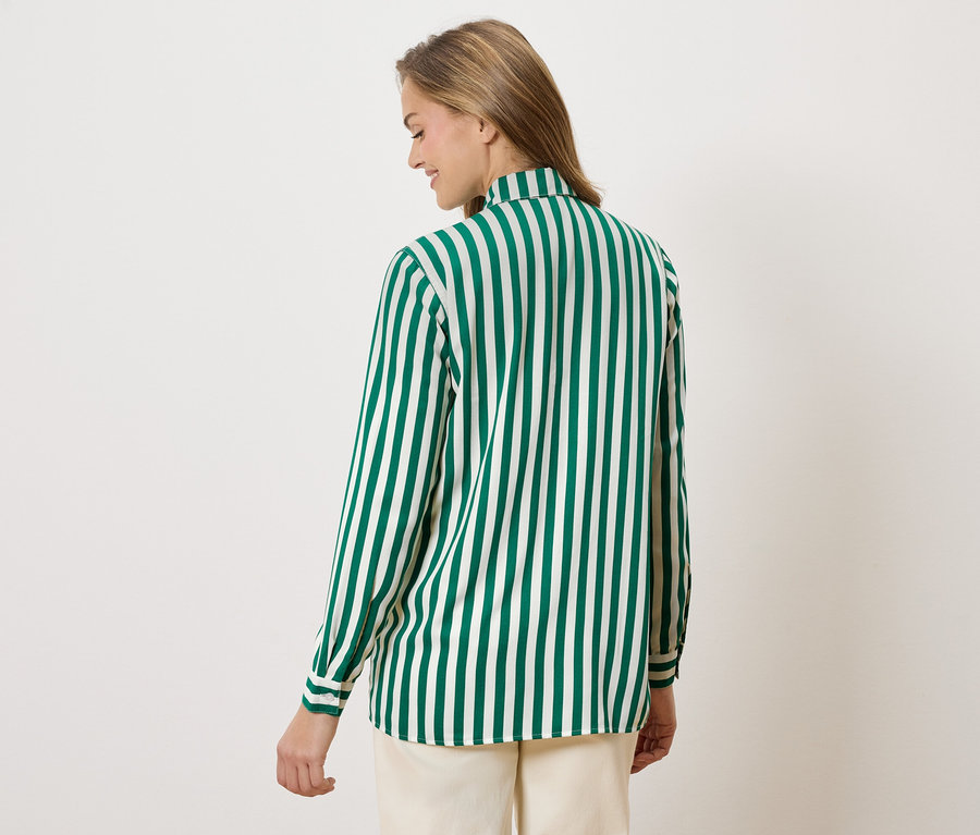Une femme vue de dos portant une chemise à rayures vertes et blanches et un pantalon beige.