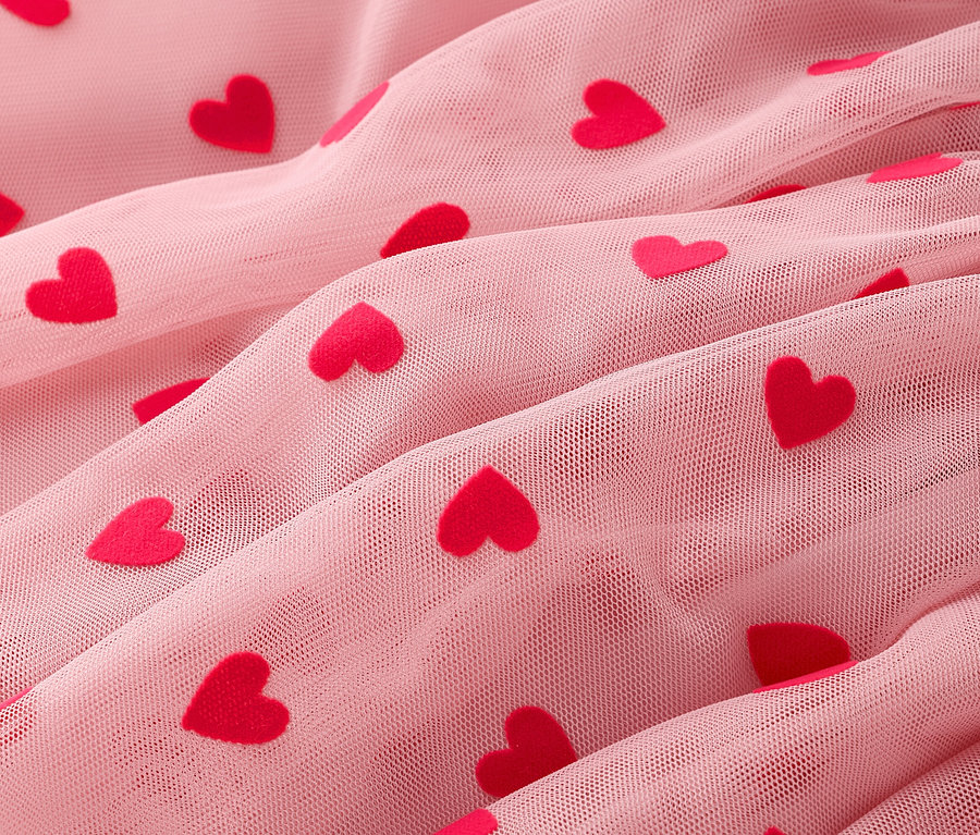 Gros plan sur un tissu en tulle rose drapé avec des cœurs rouges.