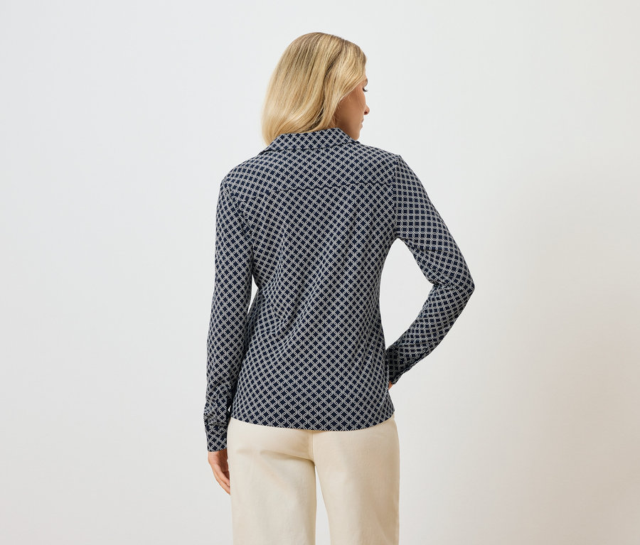 Vue arrière d'une femme blonde portant un chemisier à manches longues à motifs bleus et un pantalon clair.