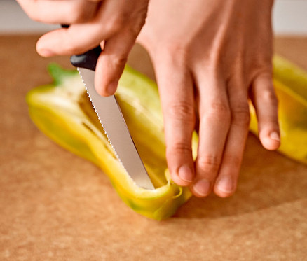 Des mains coupent un poivron jaune avec un couteau sur une planche à découper.