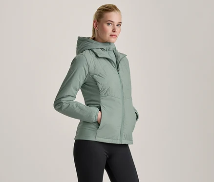 Femme portant une veste à capuche vert clair et un legging noir, les mains dans les poches de la veste.