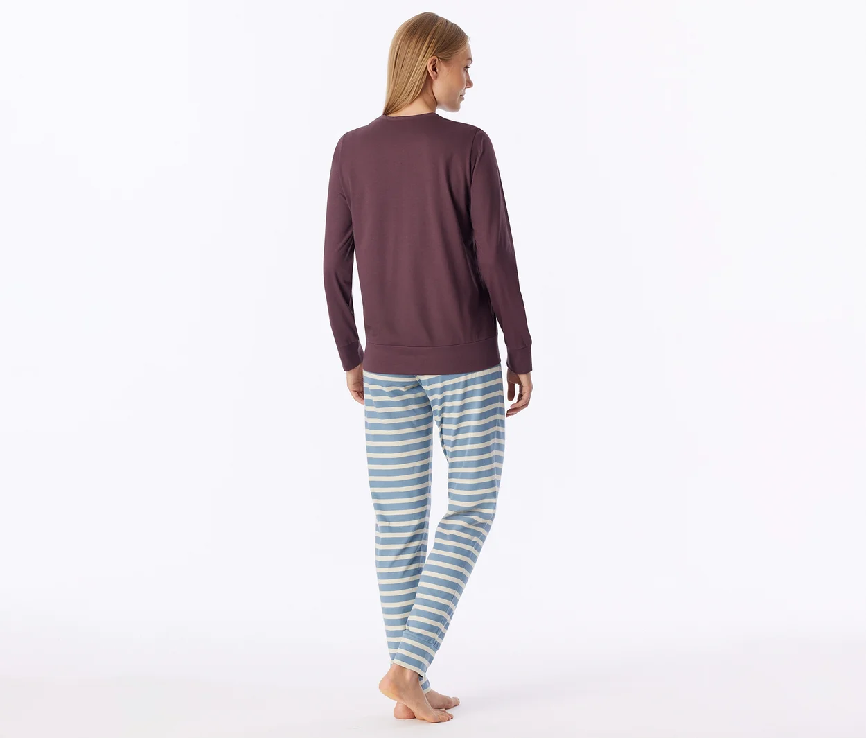 Femme vue de dos, portant un haut à manches longues violet foncé et un pantalon de pyjama rayé bleu clair et blanc, pieds nus.
