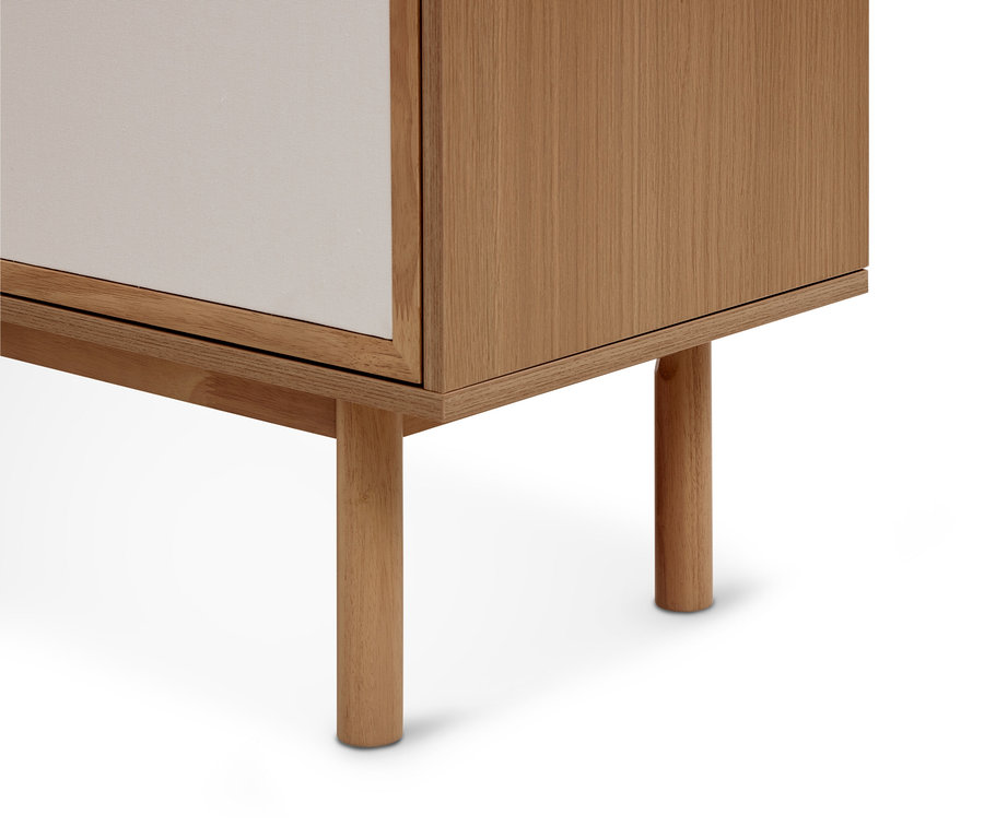 Gros plan sur le coin inférieur droit d'un meuble en bois clair avec une porte blanche, reposant sur deux pieds ronds en bois.