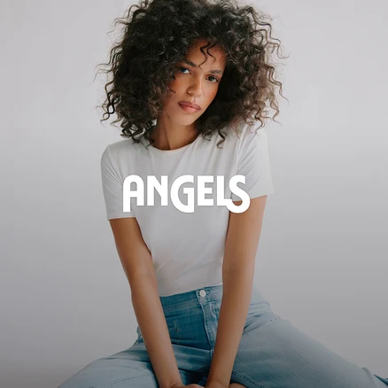 Femme aux cheveux bouclés portant un t-shirt blanc et un jean bleu clair, assise et regardant l'appareil photo. Le mot ANGELS est superposé sur l'image.