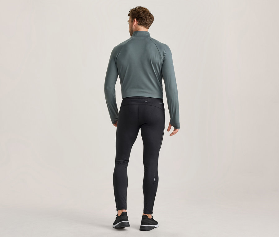 Homme vu de dos, portant un haut de sport à manches longues et col zippé de couleur sarcelle foncé, un legging de course noir ajusté avec des détails réfléchissants et des chaussures de sport noires et blanches.