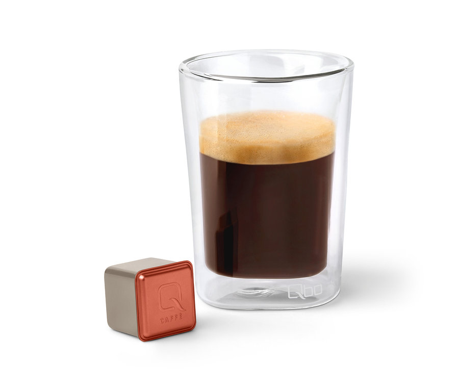 Une capsule de café Qbo Caffè TERRENO ALTO à côté d'un verre de café.