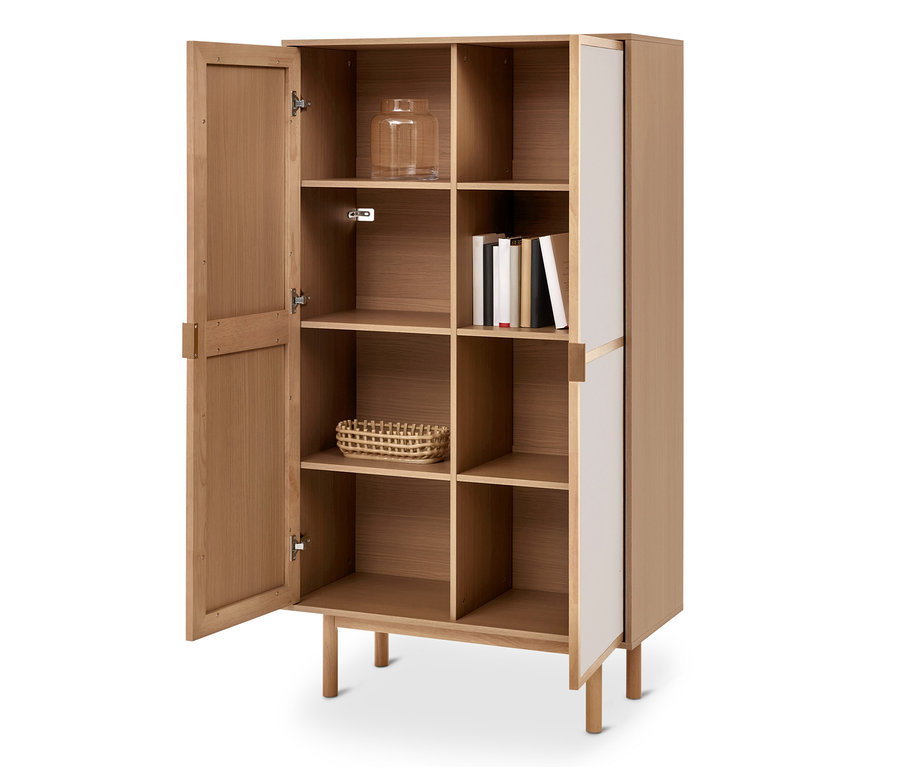 Armoire en bois clair avec une porte ouverte à gauche, révélant des étagères. À l'intérieur, un bocal en verre, des livres et un panier tressé sont visibles. Le côté droit a des panneaux blancs.