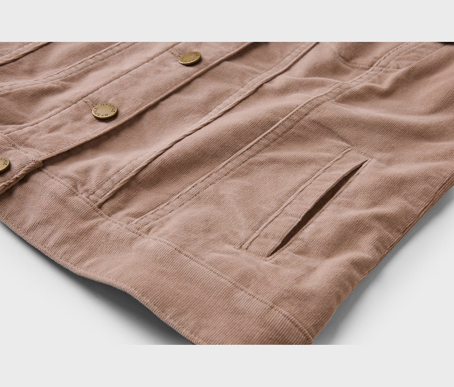 Gros plan d'une veste en velours côtelé marron clair, montrant sa texture côtelée, ses boutons dorés et une poche latérale.