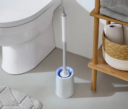 Dans la salle de bain, des toilettes blanches sont à côté d'une brosse WC avec une lumière bleue et d'une étagère en bois avec des serviettes et du papier toilette.