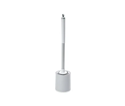 Une brosse de toilette grise avec un manche argenté et un support sur fond blanc.