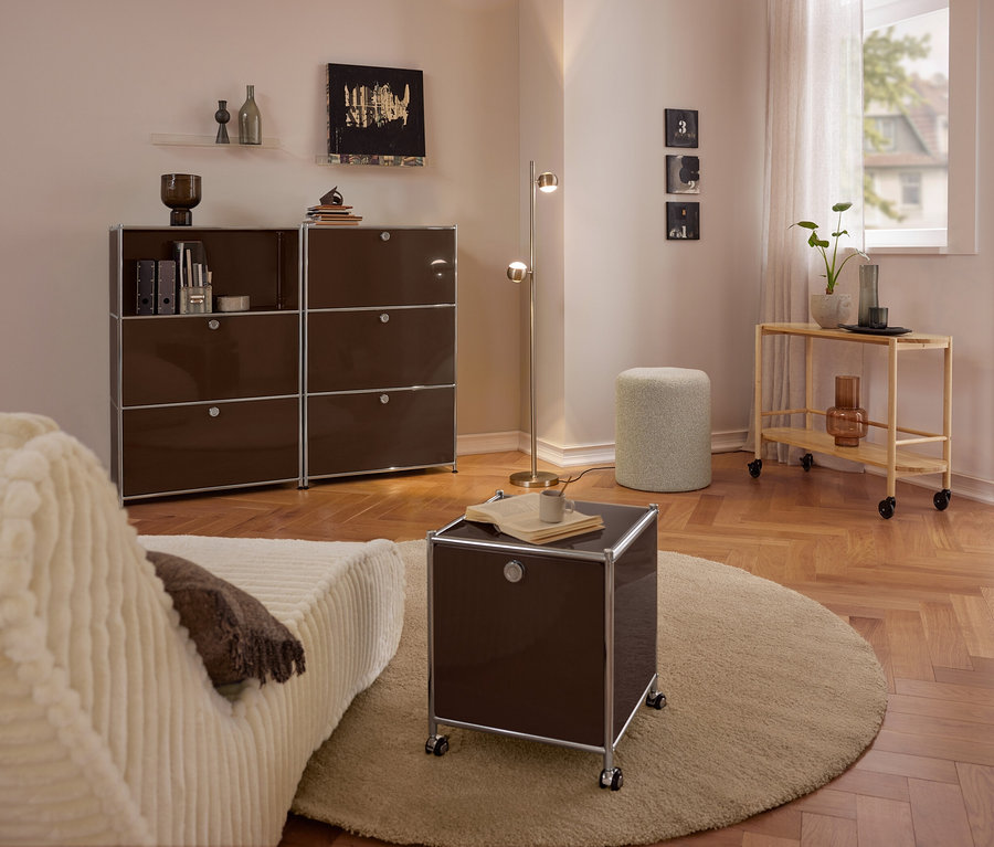 Salon moderne avec canapé beige, grande commode métallique marron »CN3« à 3 compartiments rabattables, petite commode métallique roulante marron »CN3« à 2 compartiments rabattables sur tapis rond, pouf bouclé et chariot de service en bois.