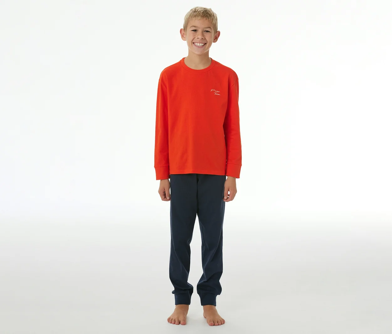 Garçon souriant portant un pyjama orange à manches longues et un pantalon de pyjama bleu marine avec des poignets.