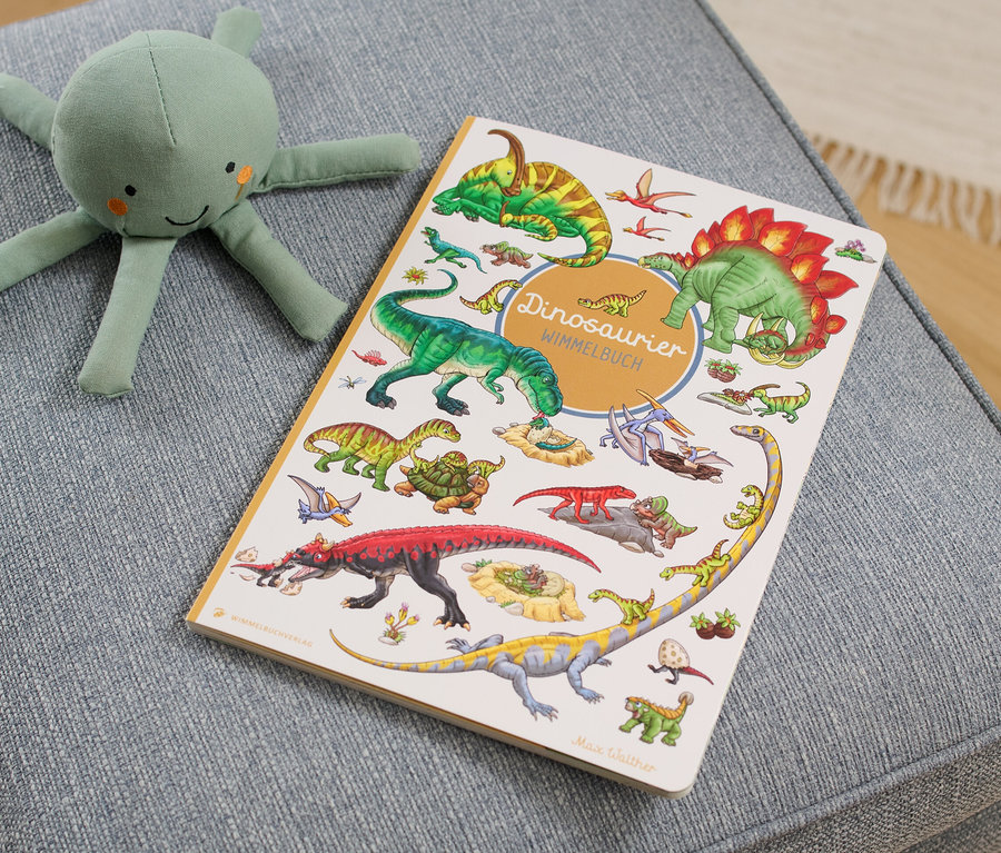 Sur un tabouret gris sont posés un livre « Dinosaurier Wimmelbuch » et une peluche de pieuvre verte.