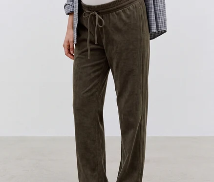 Femme enceinte debout, portant un pantalon en velours côtelé MAMALICIOUS « JACIA » vert foncé avec un cordon de serrage, un haut blanc et une chemise à carreaux, montrant son ventre.