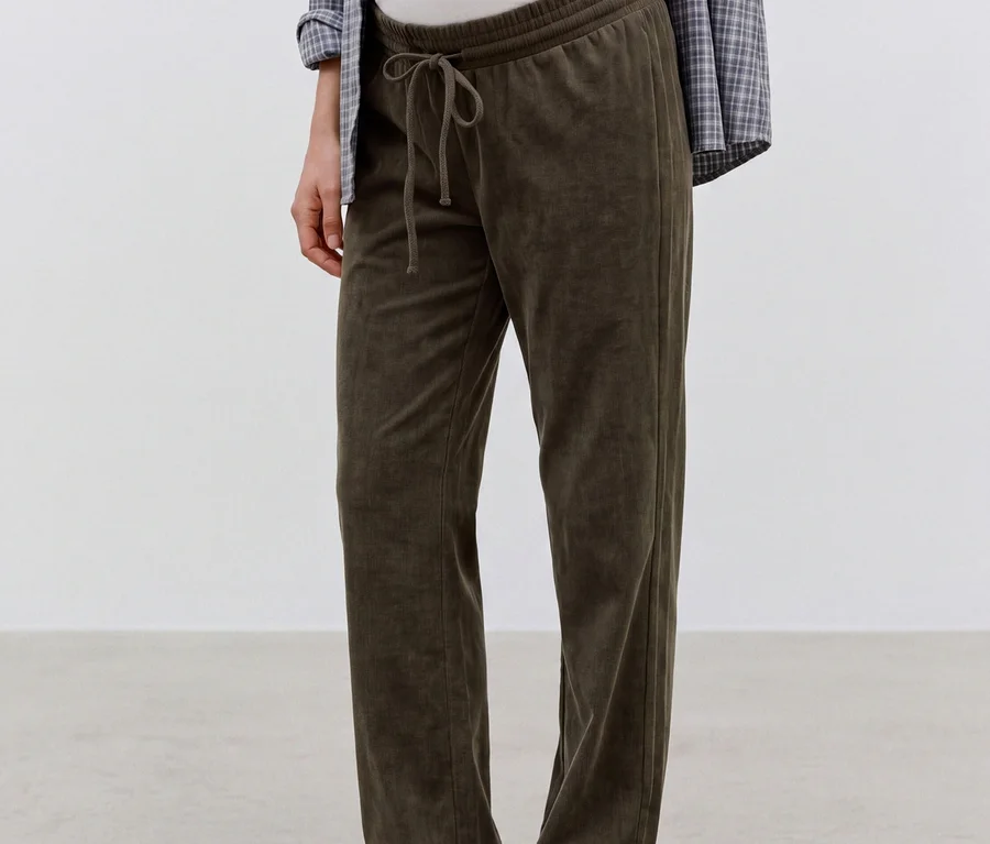 Femme enceinte debout, portant un pantalon en velours côtelé MAMALICIOUS « JACIA » vert foncé avec un cordon de serrage, un haut blanc et une chemise à carreaux, montrant son ventre.