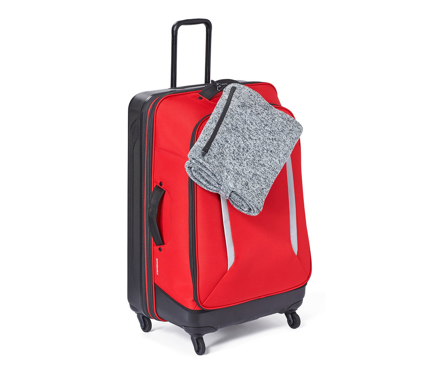 Valise rouge avec couverture de voyage sur le dessus.