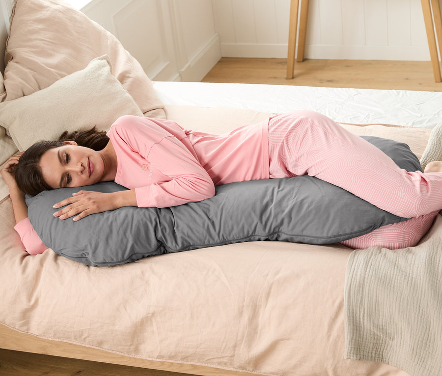 Femme allongée sur le côté sur un lit, enlaçant un coussin XL pour dormir sur le côté.