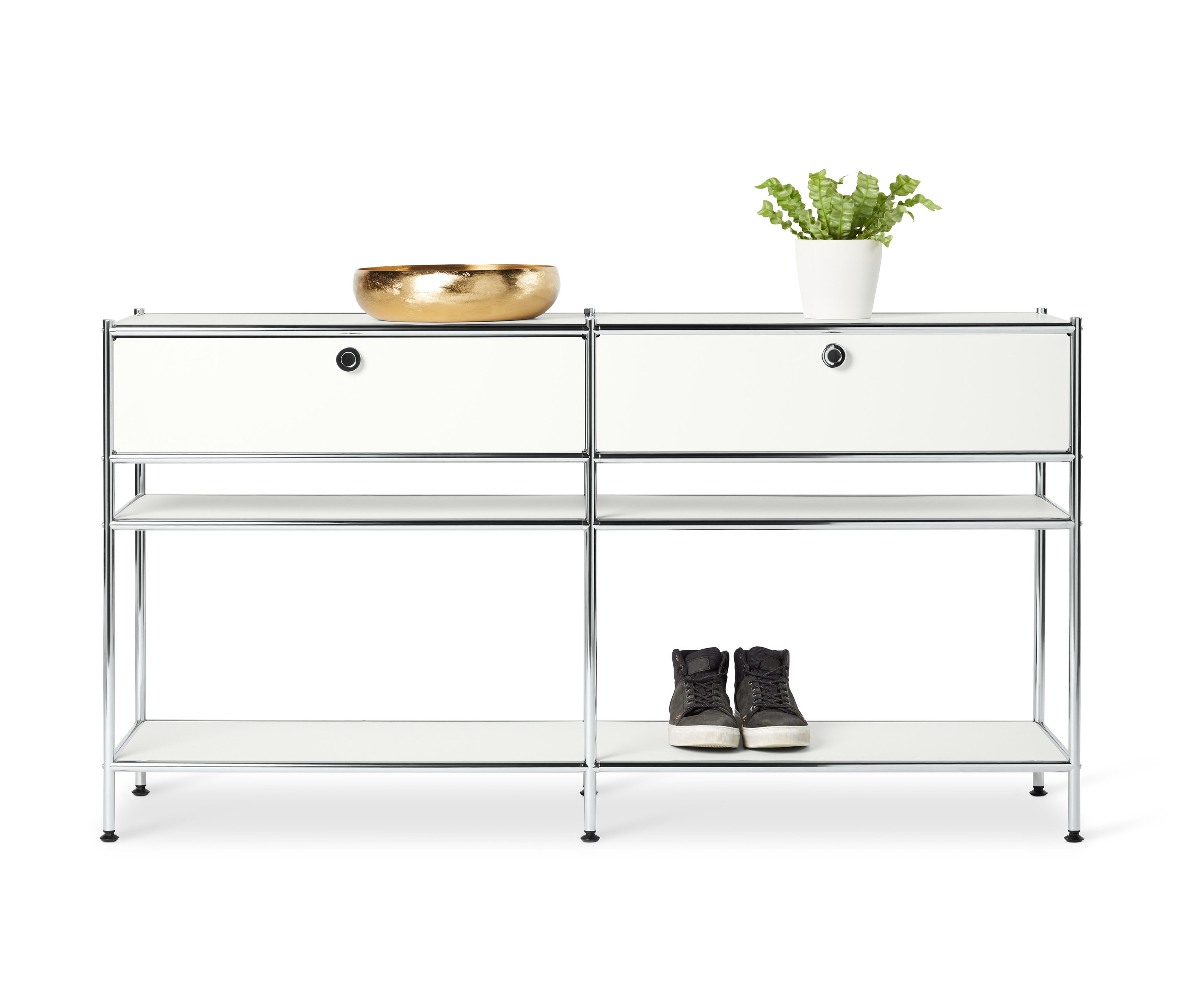Deux consoles en métal blanc « CN3 » avec 2 tiroirs chacune sont placées l'une à côté de l'autre. Sur le dessus de la console gauche se trouve un bol doré et sur le dessus de la console droite une plante dans un pot blanc. Des chaussures sont posées sur l'étagère inférieure.