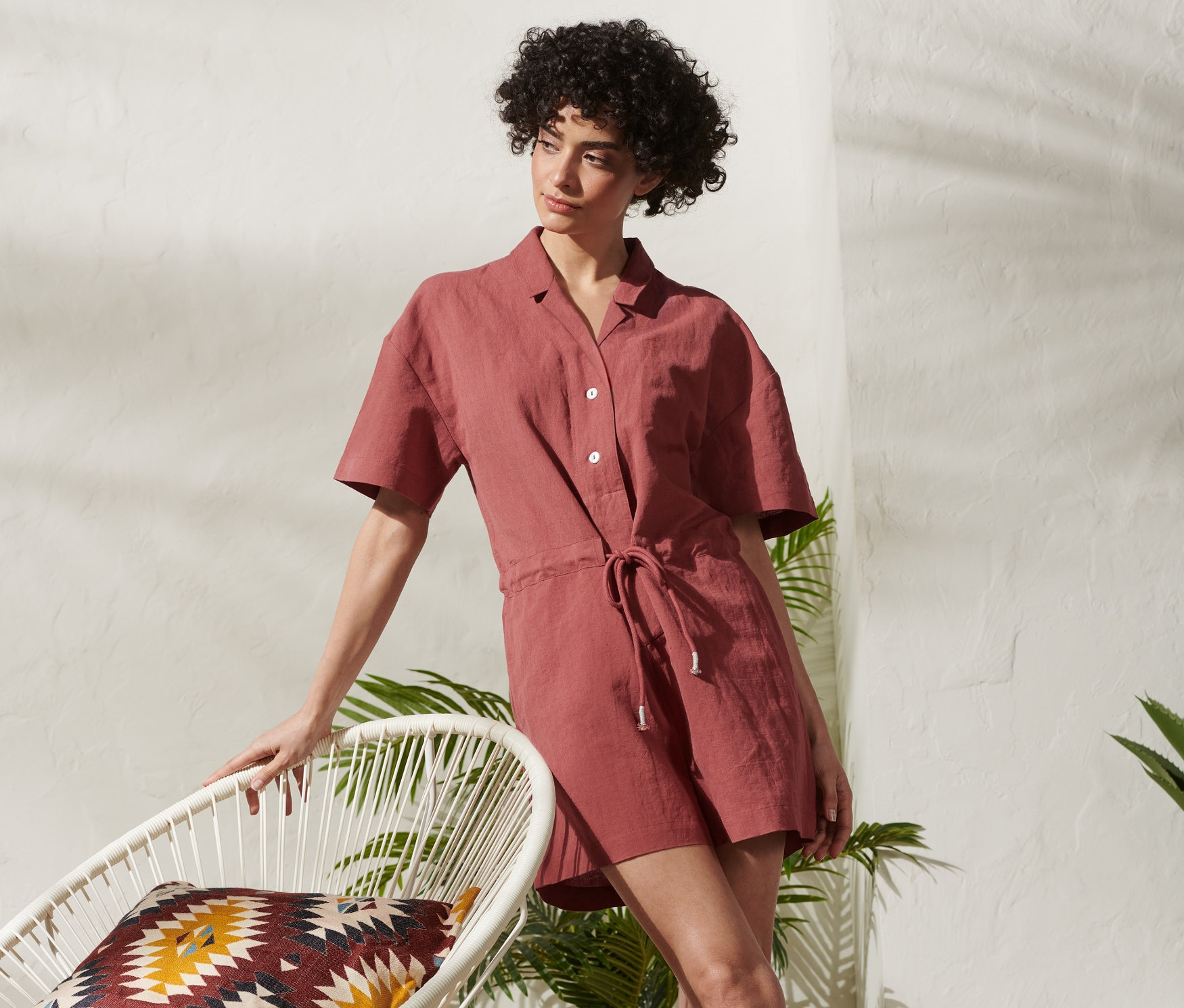 Femme appuyée sur une chaise blanche en combinaison courte en lin mélangé.