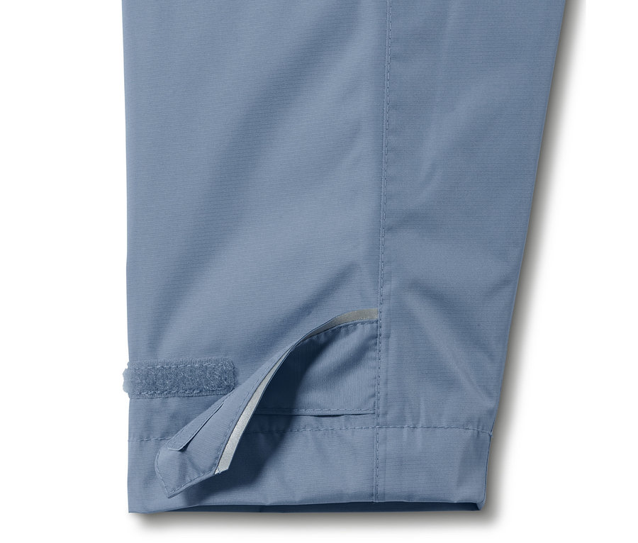 Gros plan sur une veste de pluie unisexe bleue, avec un détail de la manchette à velcro visible.