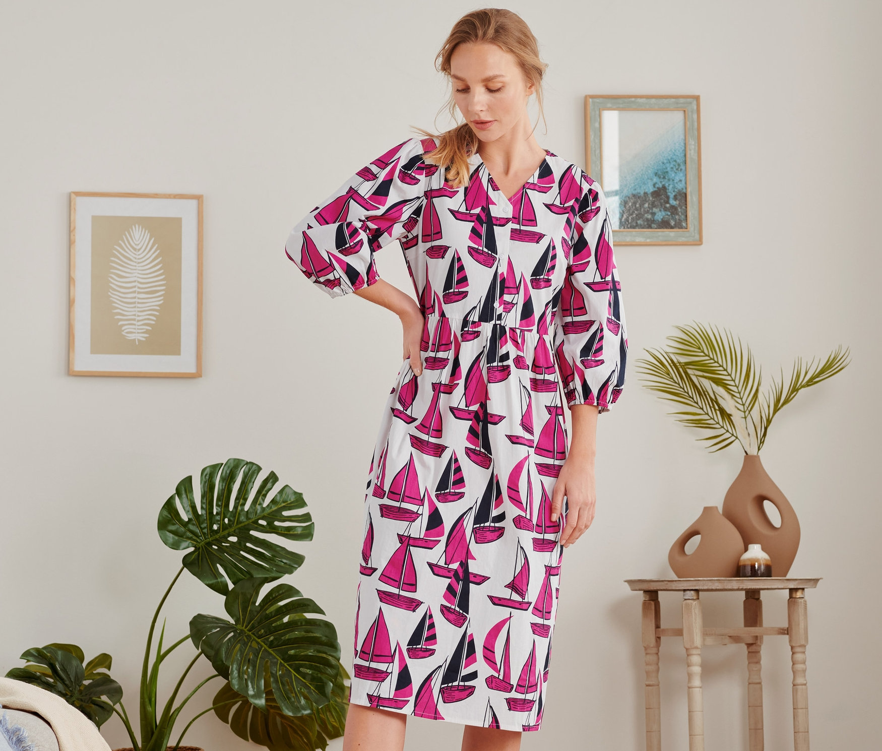 Une femme se tient dans une pièce et porte une robe midi à imprimé de voiliers.