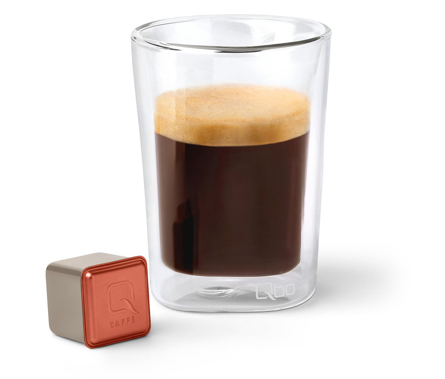 Une capsule de café Qbo Caffè TERRENO ALTO à côté d'un verre de café.