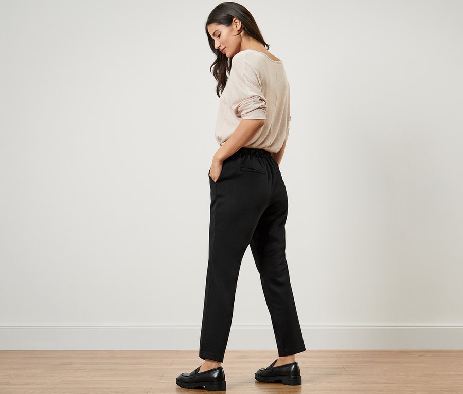 Femme portant un pull beige et un pantalon de jogging noir.