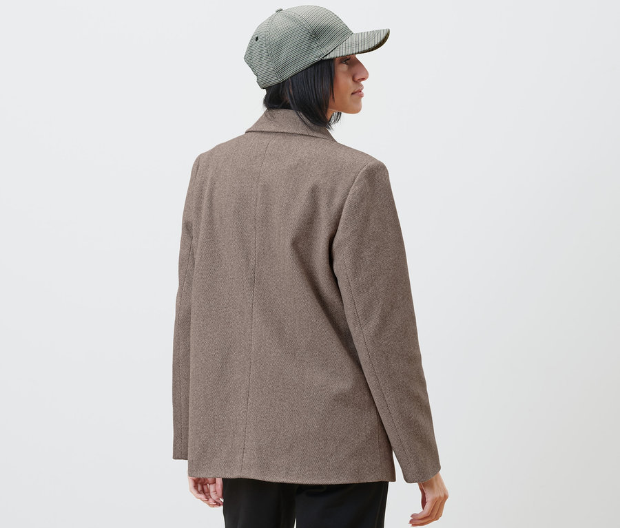 Femme portant un blazer et une casquette à carreaux regardant vers la droite.