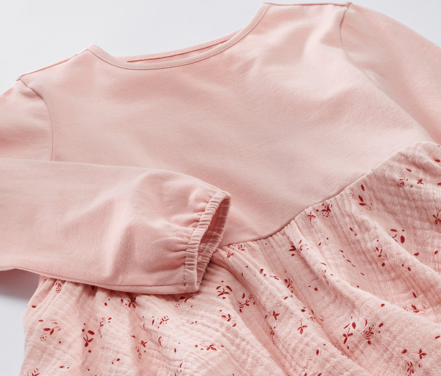 Gros plan sur une robe tissée rose pour enfant, avec des manches longues et un motif floral sur la jupe.