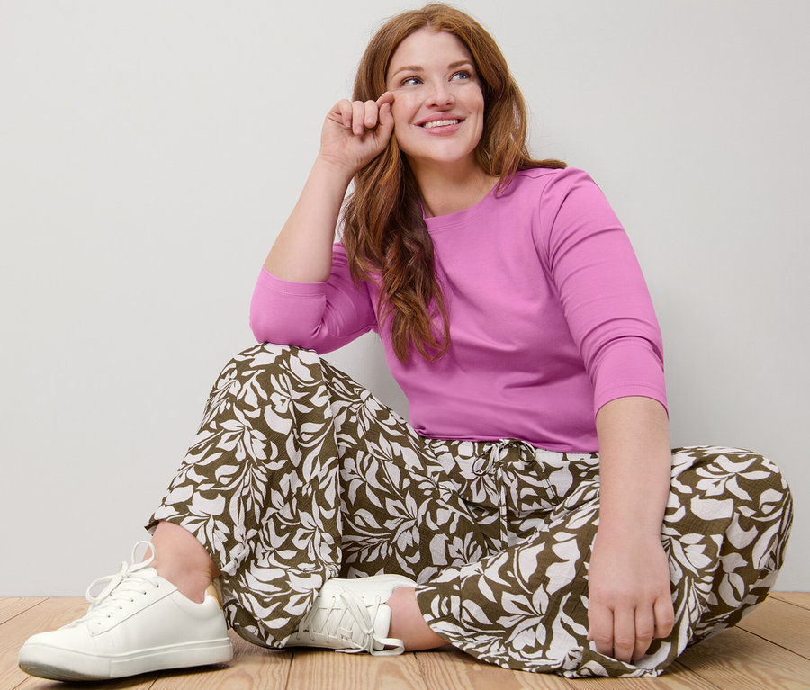 Femme assise par terre portant un tee-shirt rose à manches 3/4 et un pantalon imprimé à taille élastique.