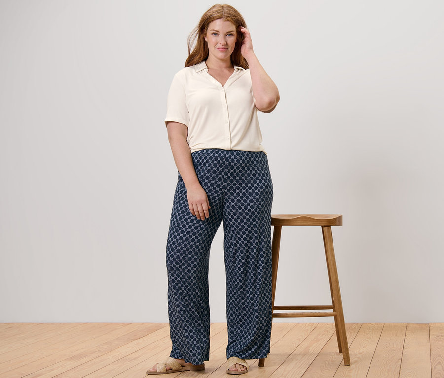 Femme posant dans une blouse blanche avec patte de boutonnage et un pantalon palazzo imprimé bleu foncé.
