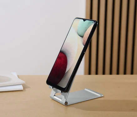 Un smartphone noir est posé sur un support pour smartphone et tablette sur une table.