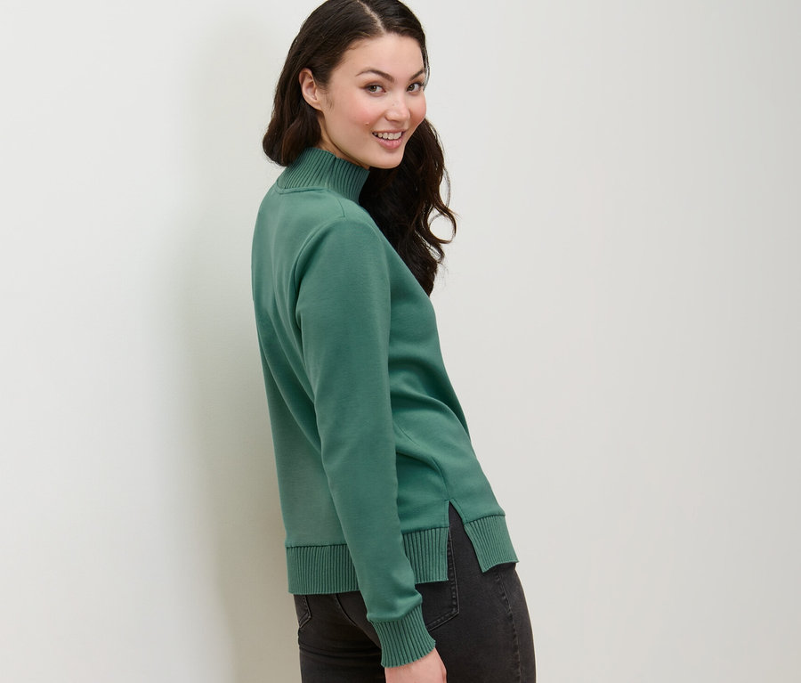 Femme regardant par-dessus son épaule portant un sweatshirt vert avec col montant.