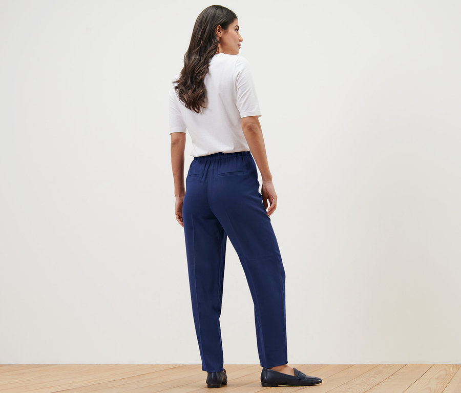 Une femme, vue de dos, porte un t-shirt blanc et un pantalon tissé.