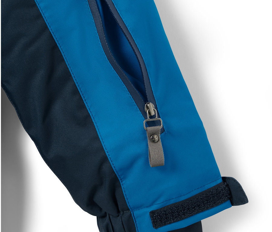 Gros plan sur une veste de ski pour enfant bleu et bleu marine avec une poche zippée sur la manche.