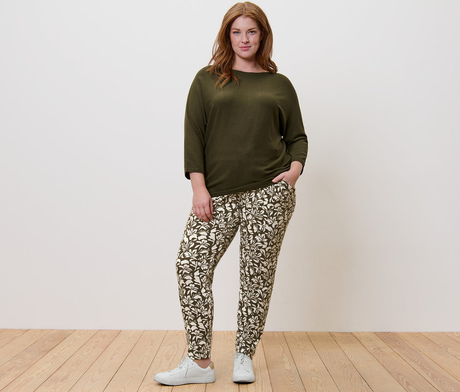 Une femme debout porte un pull en maille fine vert et un pantalon en jersey imprimé.