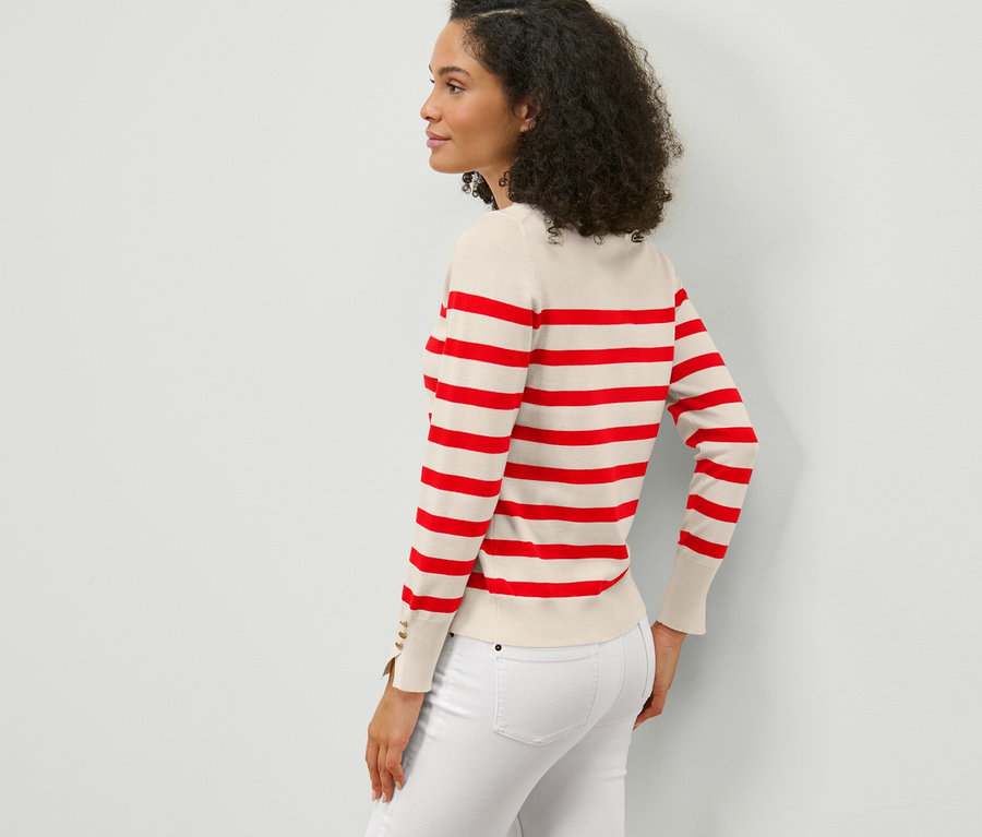 Vue de côté d'une femme aux cheveux bouclés foncés portant un pull en maille fine rayé rouge et un jean blanc.