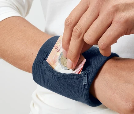 Une main met un billet d'euro et une pièce dans un porte-monnaie de sécurité bleu pour le poignet.