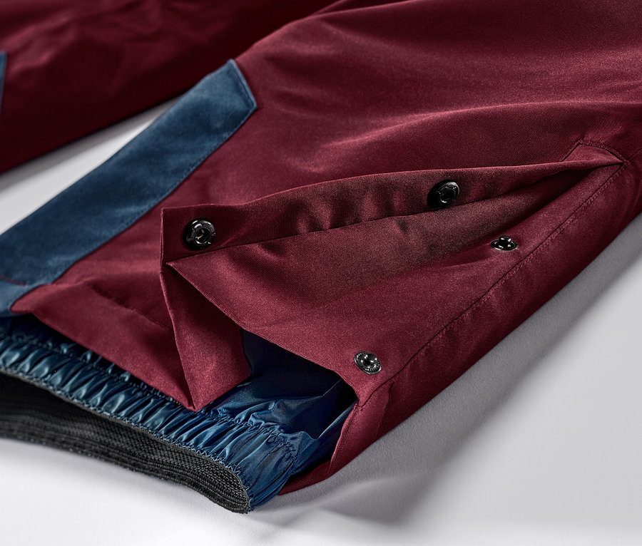 Gros plan sur un pantalon de ski et de snowboard bordeaux avec des accents bleus et une fermeture boutonnée.