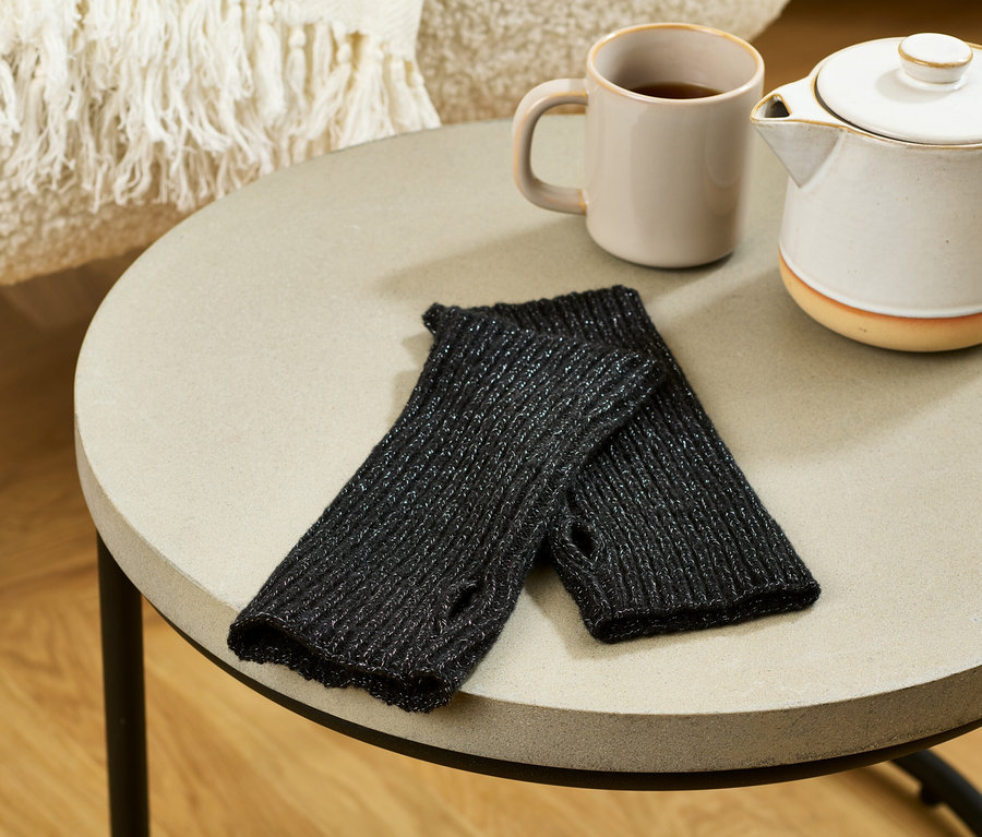 Sur une table, des manchettes en maille scintillantes sont posées à côté d'une tasse et d'une théière.