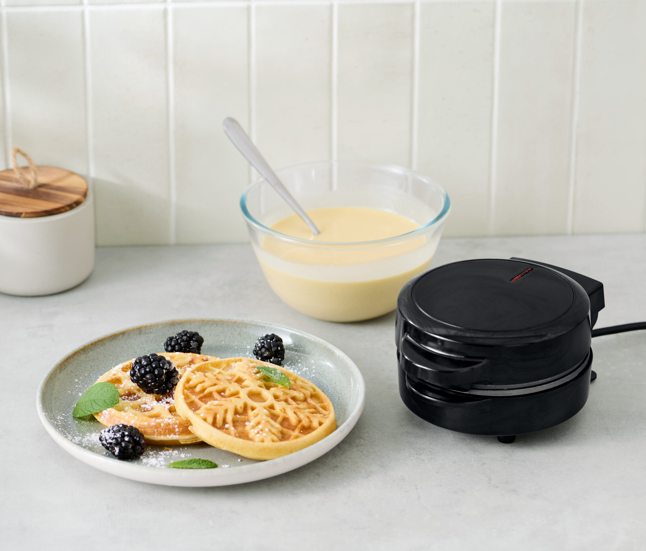 Mini-gaufrier à côté d'une assiette de gaufres, de mûres et de menthe.