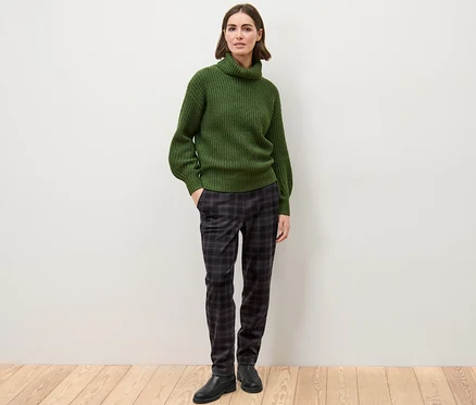 Une femme debout porte un pull vert et un pantalon de jogging à carreaux.