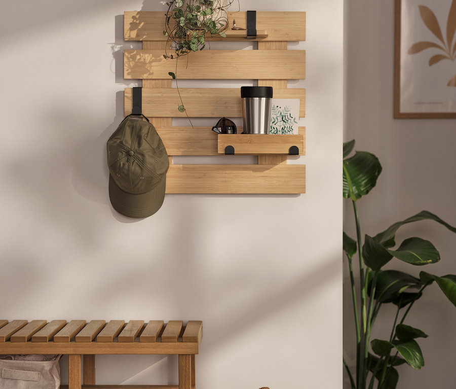 Un support mural avec des crochets flexibles et une étagère est accroché au mur. Il y a une plante, une gourde et une carte dessus. Une casquette est accrochée à l'un des crochets.