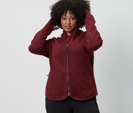 Femme ajustant ses cheveux, portant une veste en maille polaire rouge foncé et un pantalon jazz thermique.