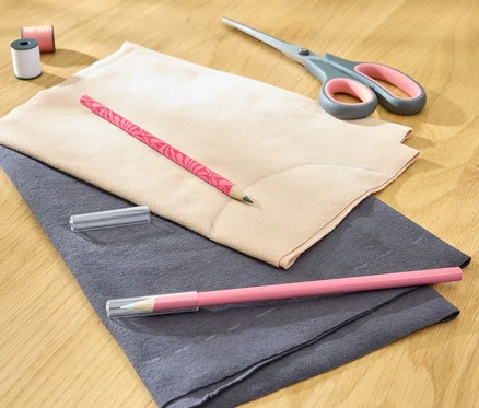 Deux crayons de craie en tissu reposent sur du tissu avec des ciseaux, du fil et une bobine.