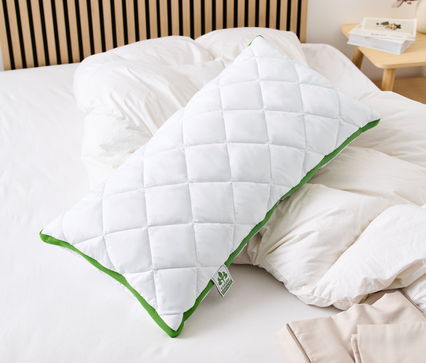 Un coussin irisette® greenline à bande thermorégulatrice blanc matelassé avec une bordure verte est posé sur un lit.
