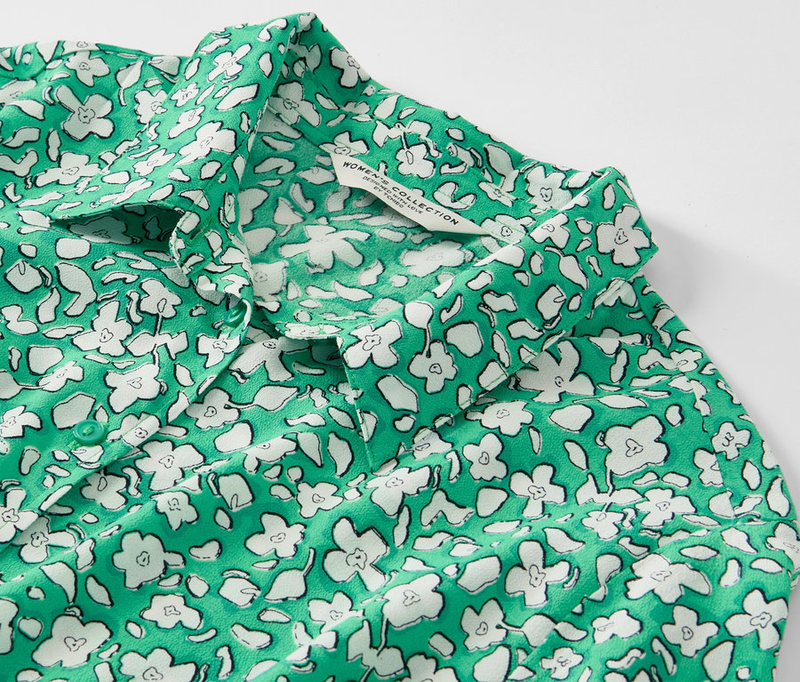 Gros plan sur une robe chemise imprimée verte avec des fleurs blanches.
