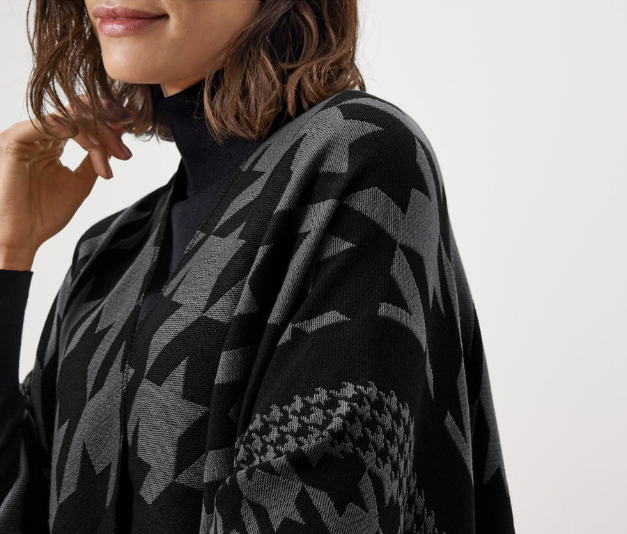 Gros plan sur une femme portant un pull à col roulé noir et une pèlerine grise et noire à motifs.