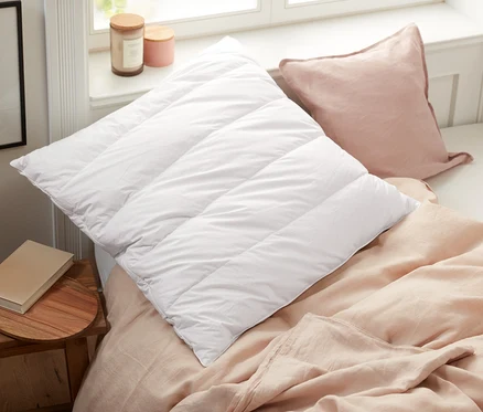 Sur un lit se trouvent un oreiller matelassé blanc et un oreiller rose à côté d'un oreiller garni de copeaux de pin cembro.