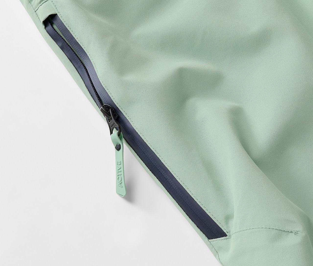 Détail d'une veste vert clair avec une fermeture éclair et un ourlet bleu foncé.